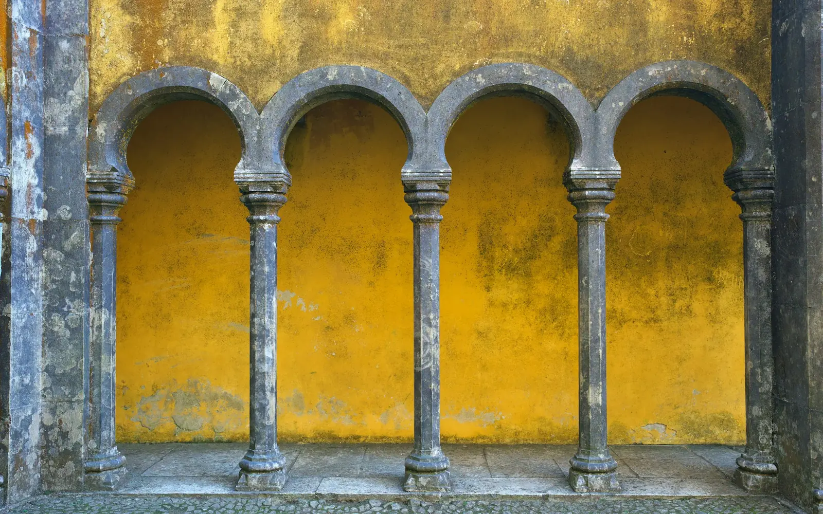 Grey stone arches set into a bright yellow wall at Pena Palace