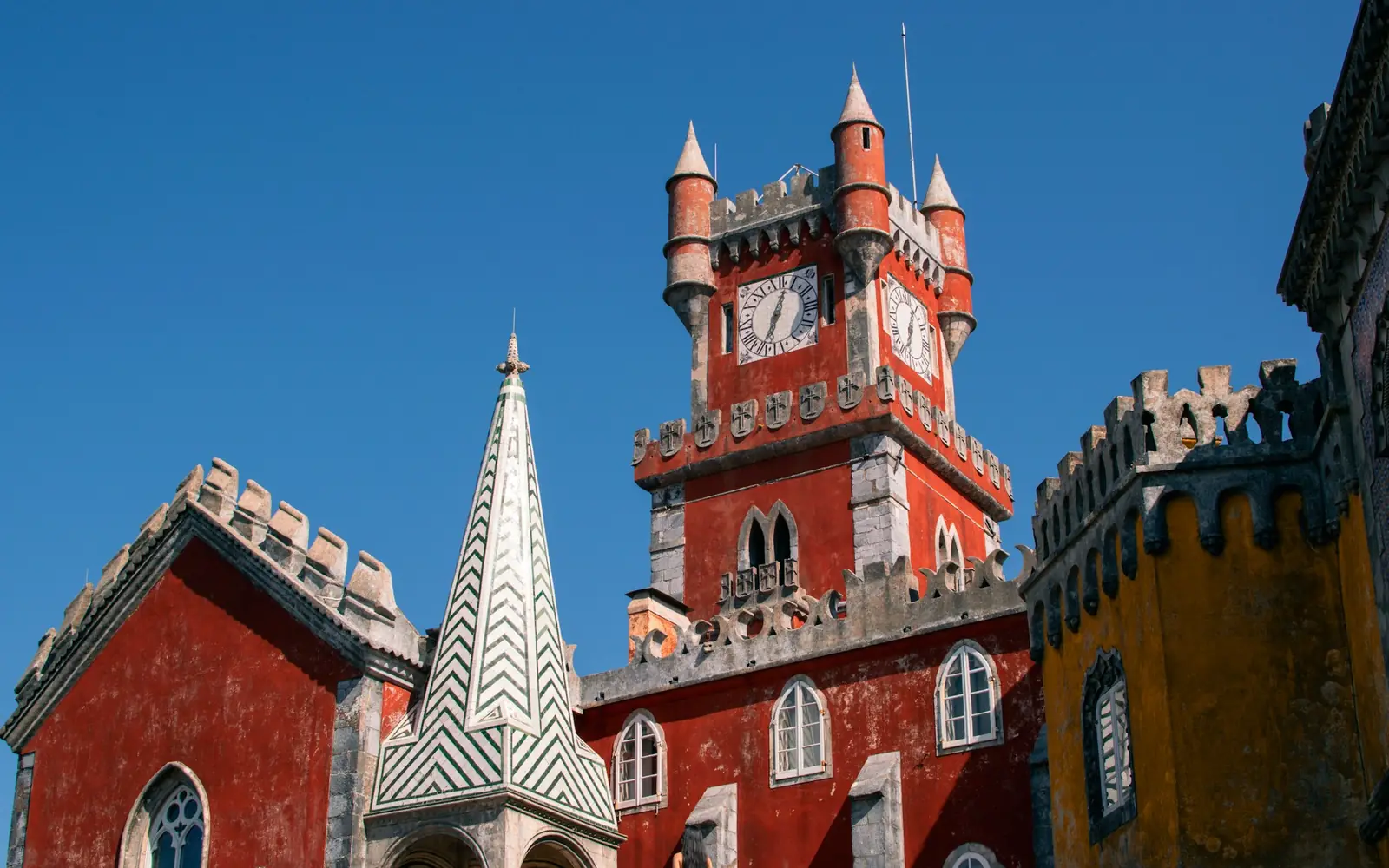 The vermilion clock-tower wing of Pena Palace against a blue sky