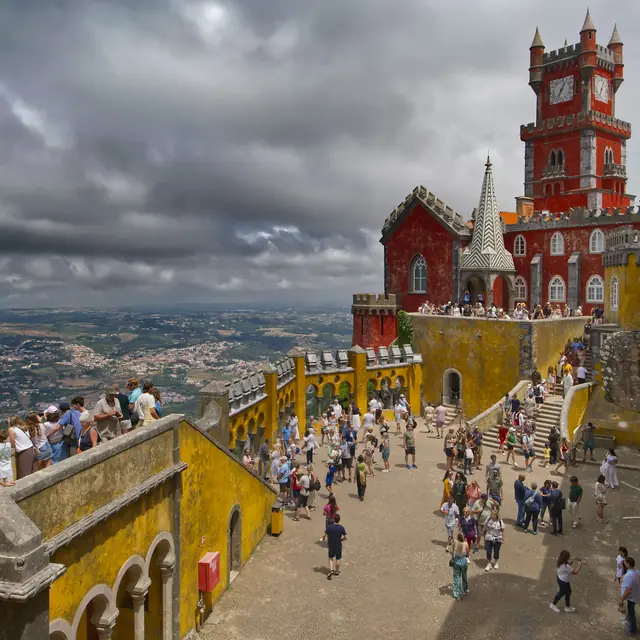 Visitors on the sunlit terraces beneath the yellow tower at Pena Palace
