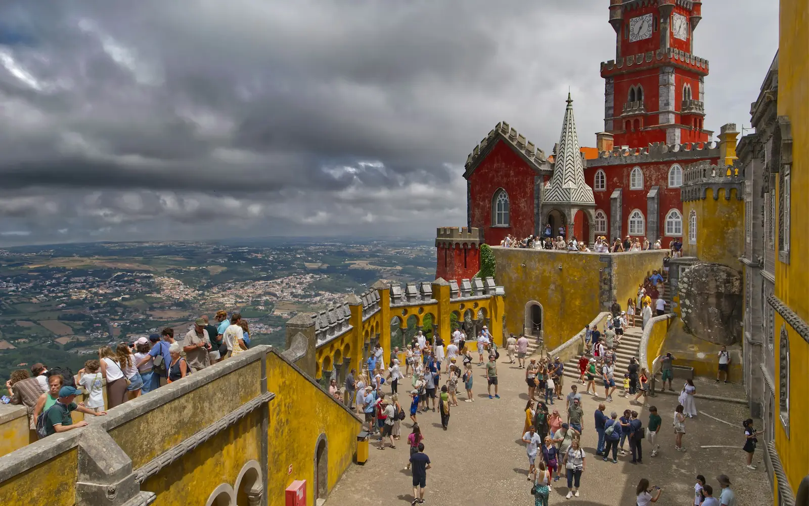 Visitors on the sunlit terraces beneath the yellow tower at Pena Palace